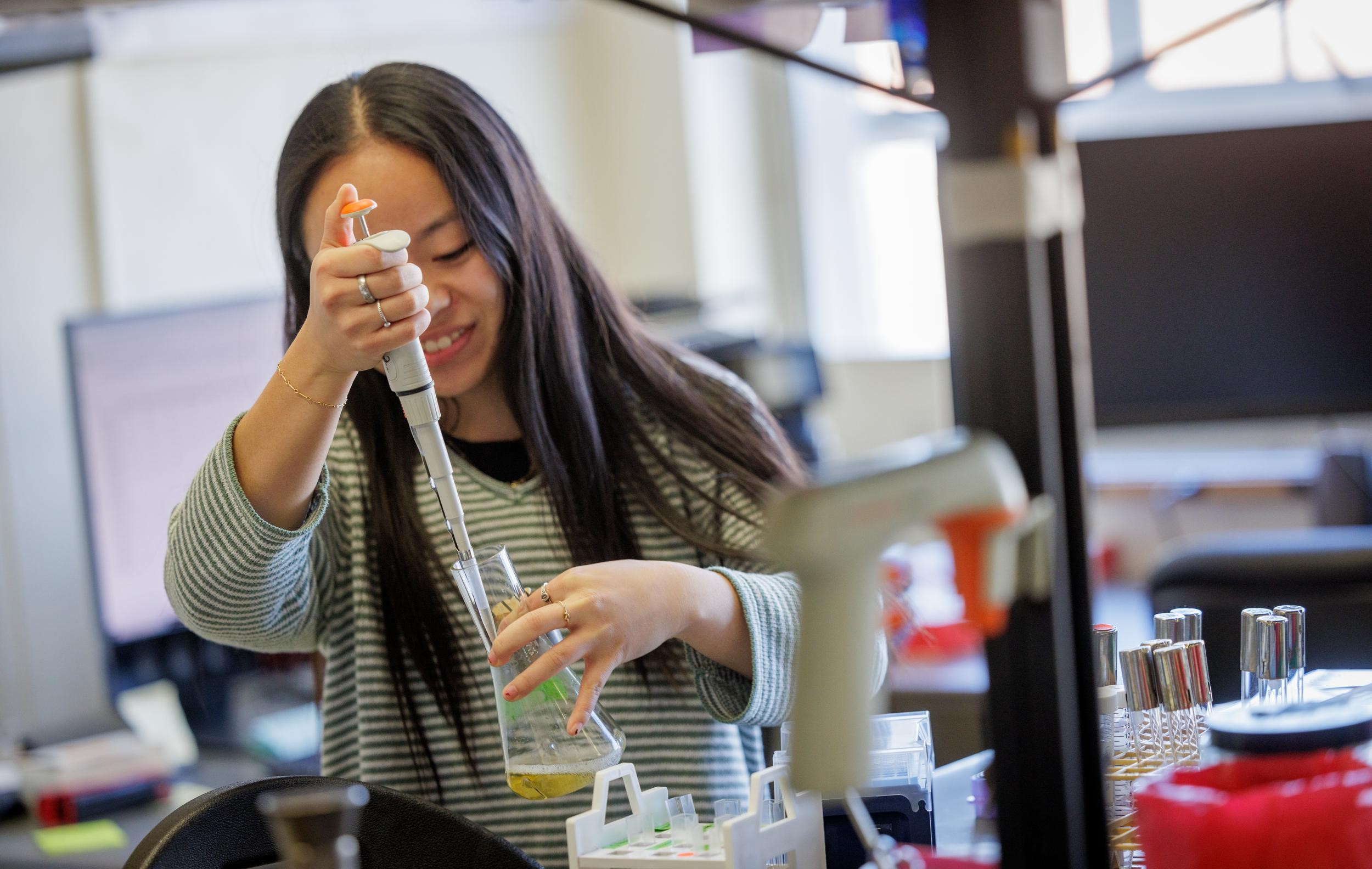 A woman is using a pipette to research microbiology